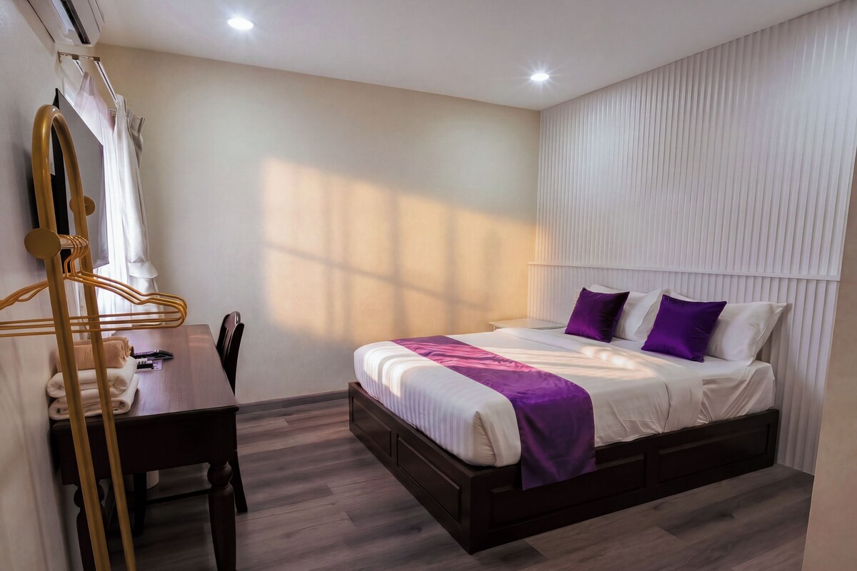A hotel room with a bed, bedside table, and a desk with a chair.