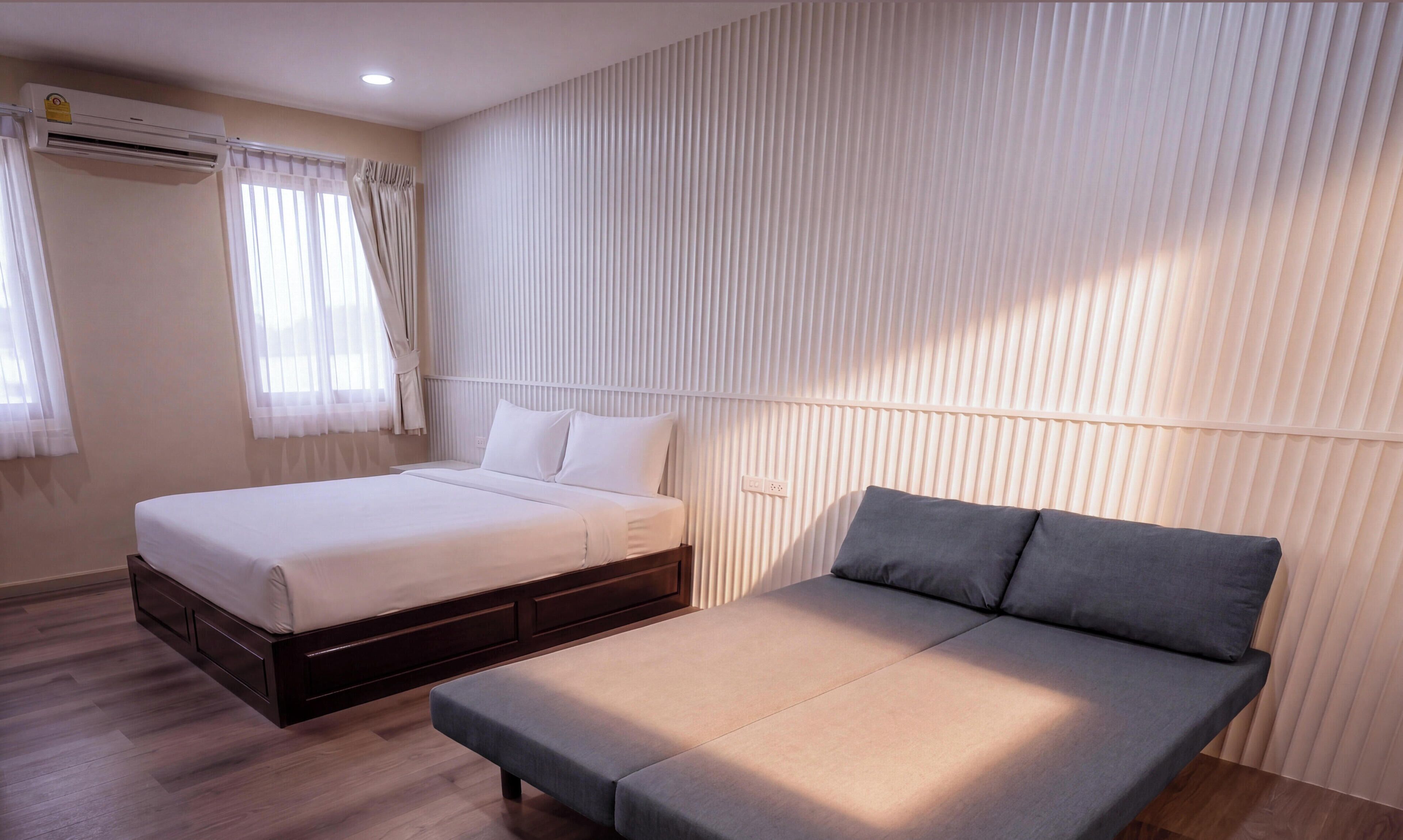 A hotel room with a bed, a sofa, a window with curtains, and an air conditioning unit.