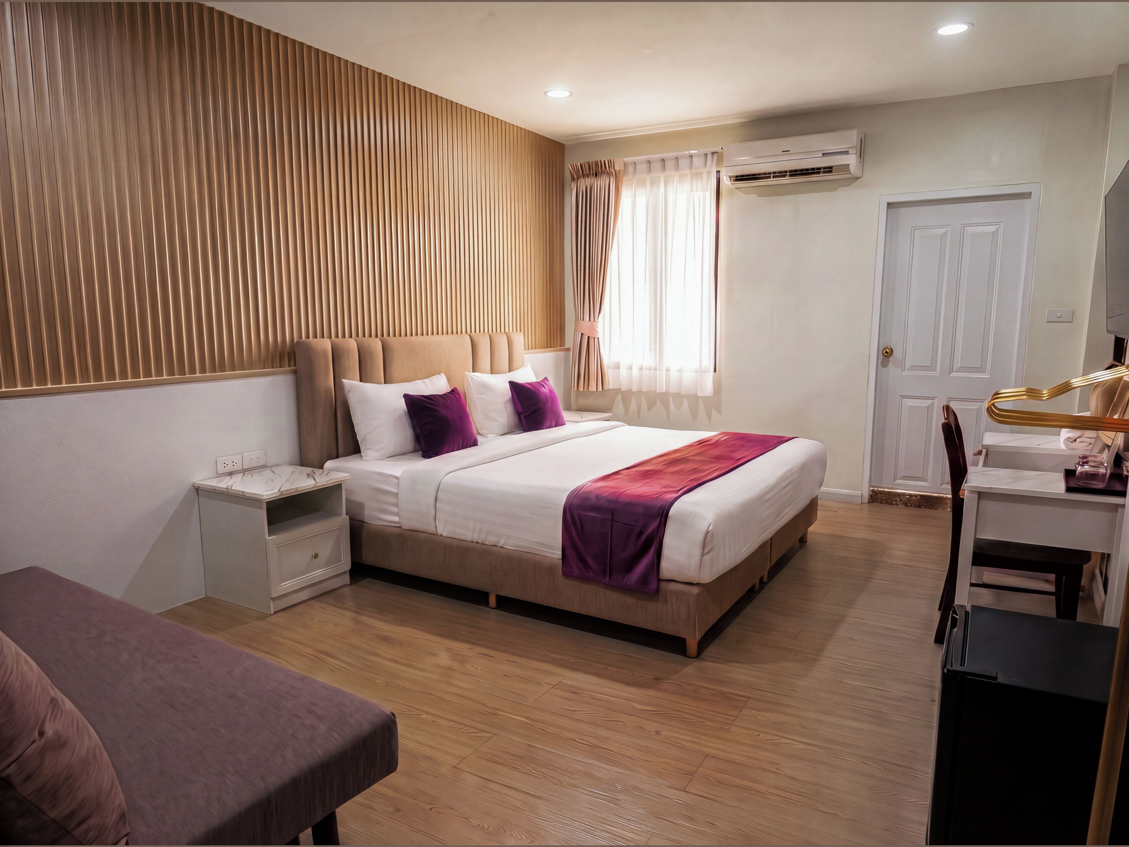 A modern bedroom with a bed, bedside tables, an air conditioning unit, a desk, and a chair.