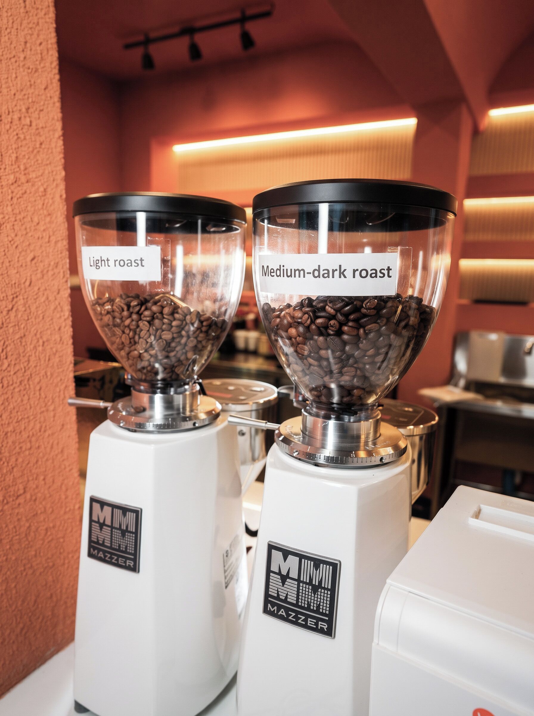 Zwei Kaffeemühlen, eine mit 'light roast' und die andere mit 'medium-dark roast' gekennzeichnet, mit einem Markenlogo am Sockel.