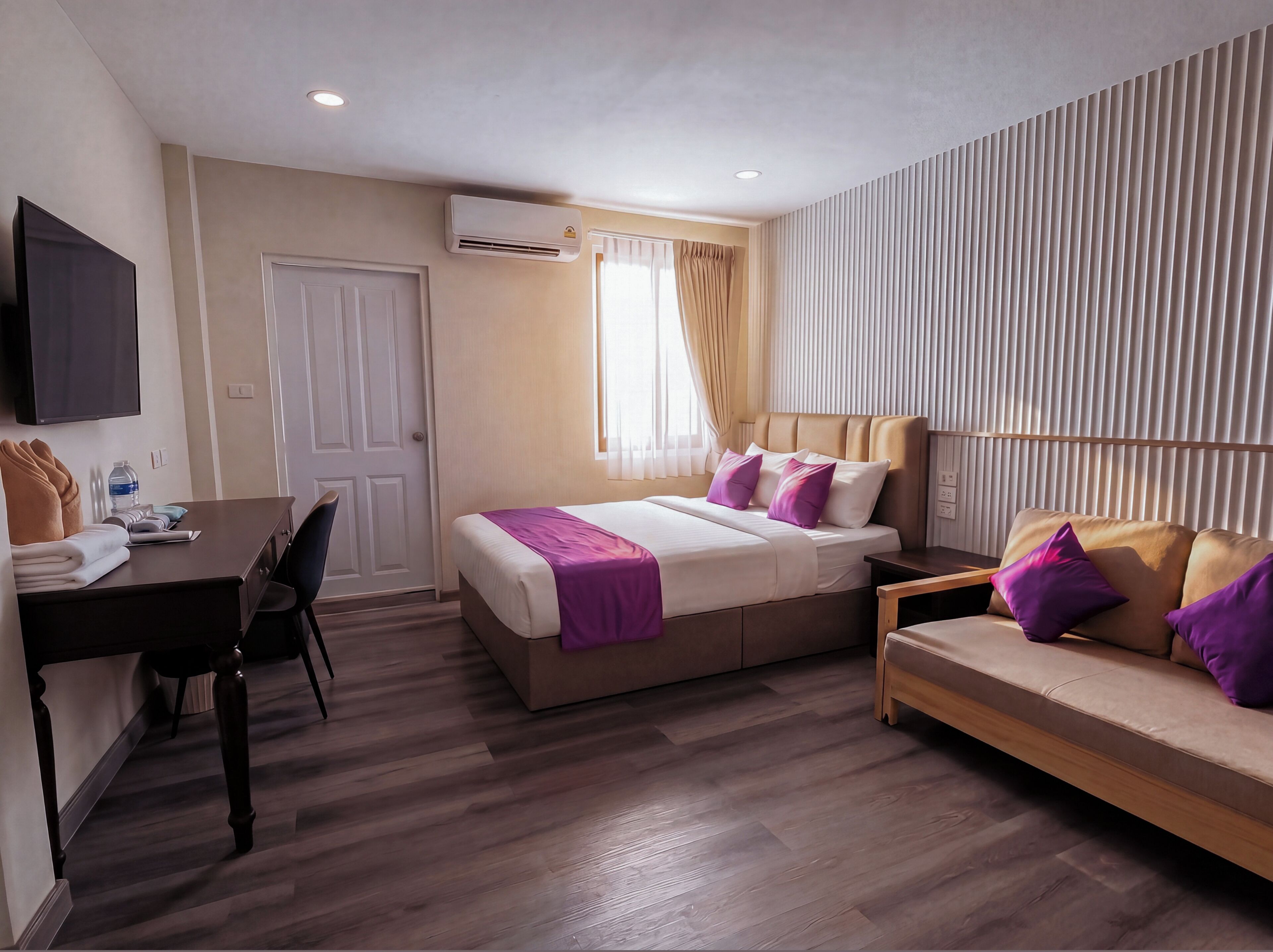 A hotel room with a bed, a sofa, a desk, and a TV.