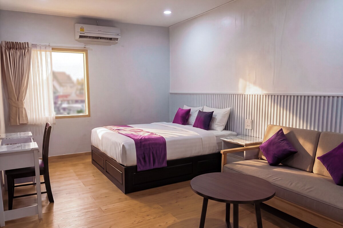 A modern hotel room with a bed, a sofa, a small table, and a desk.