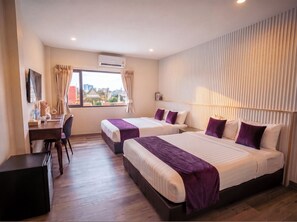 A hotel room with two beds, a desk, a chair, and a view of the city.
