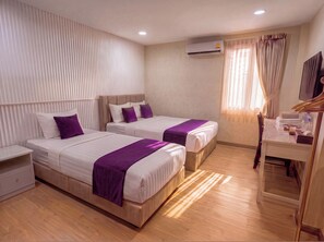 Une chambre d’hôtel avec deux lits, un bureau, un miroir et un appareil de climatisation.
