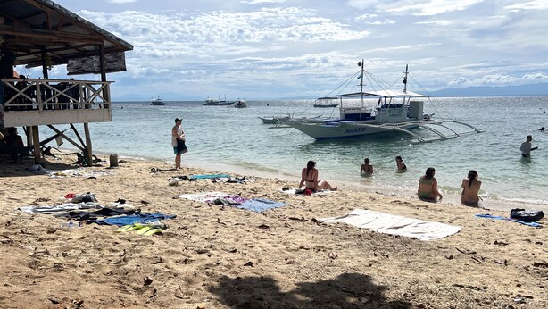 A beach with boats, a wooden structure, and people relaxing. - Neptune Diving Resort Moalboal (Moalboal)
