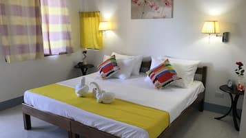 A neatly made bed with white bedding and a yellow accent, a small bedside table with a lamp, and a wall-mounted picture of flowers.