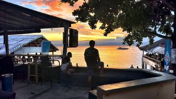 Escena costera con vista al atardecer, un muelle con gente y el letrero de un restaurante.