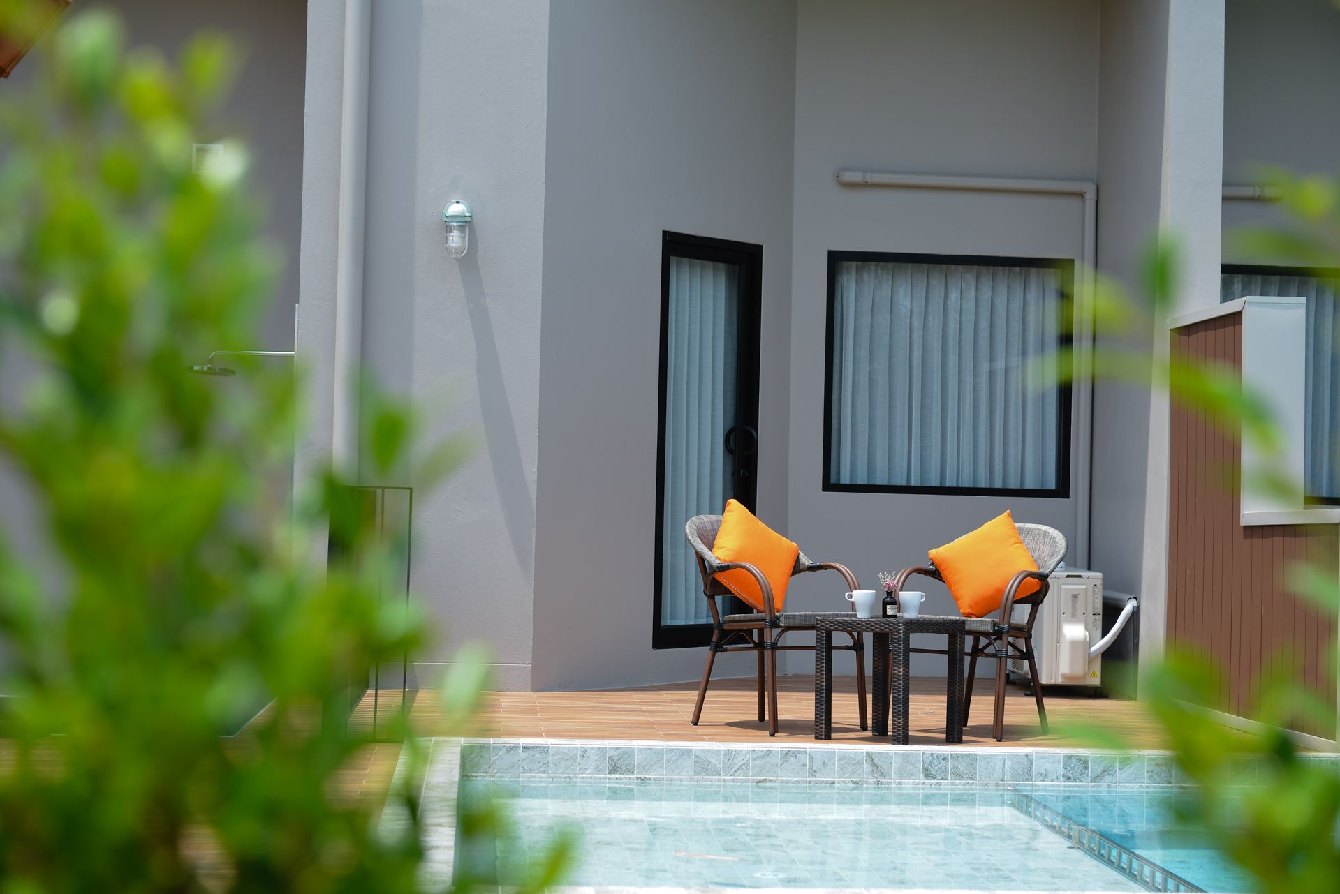 Ein moderner Außenbereich mit zwei Korbstühlen, einem kleinen Tisch, einem Pool und Blick ins Innere des Gebäudes.