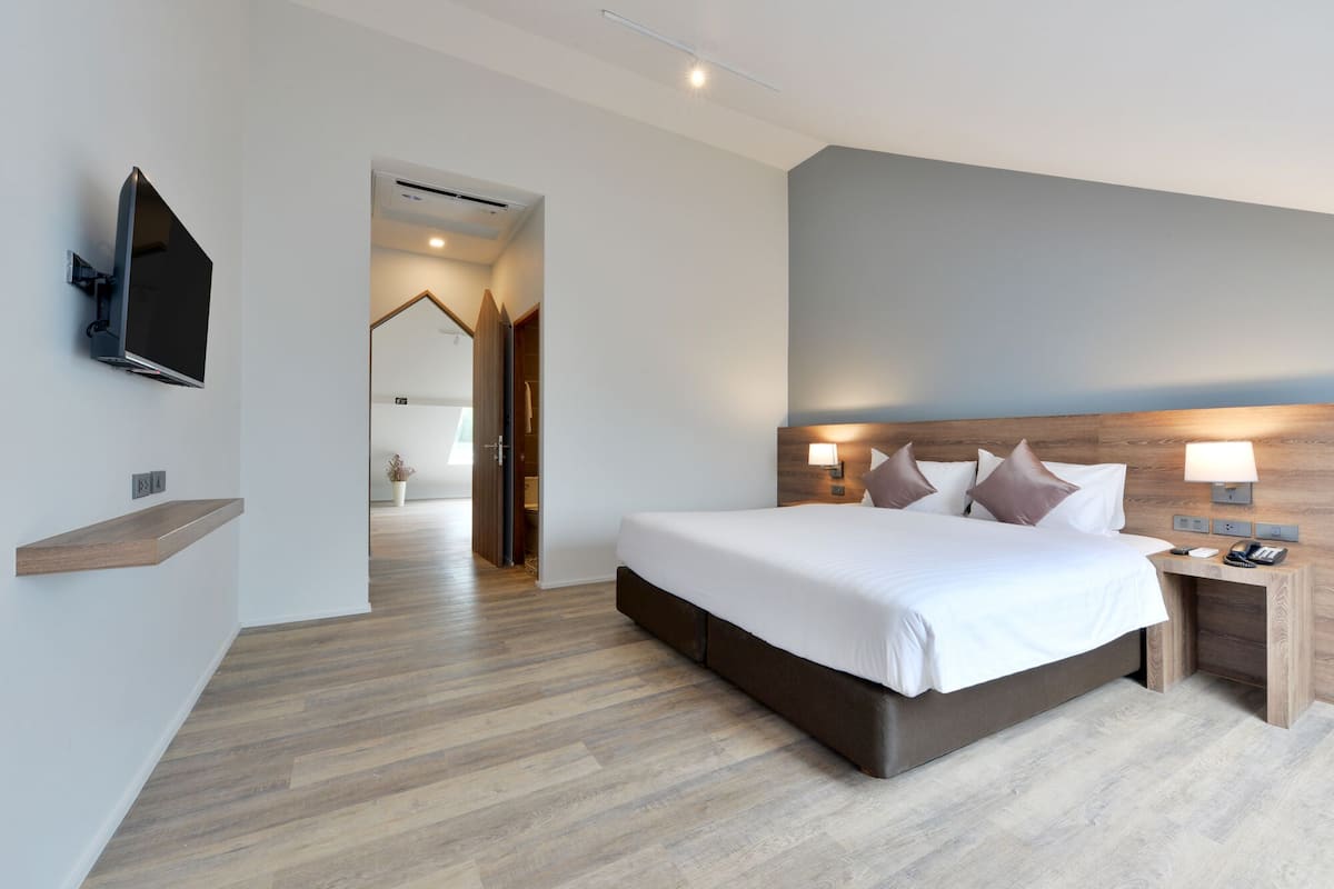 A modern hotel room with a large bed, a TV mounted on the wall, a wooden nightstand, and a built-in headboard.