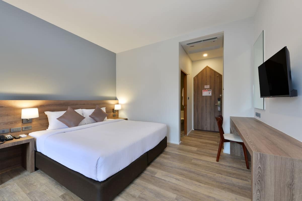 A hotel room with a bed, bedside tables, a desk, a chair, a TV, and a wooden door.
