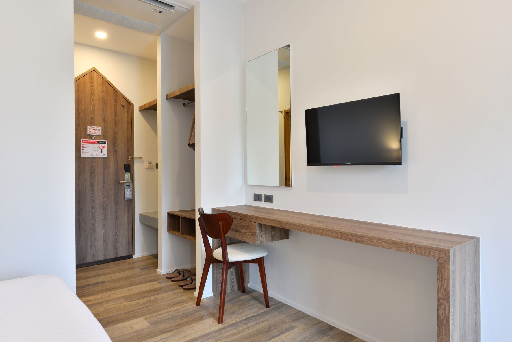 Habitación de hotel con escritorio de madera, una silla, un televisor montado en la pared y una puerta de madera.
