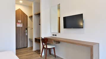 A hotel room with a wooden desk, a chair, a TV mounted on the wall, and a wooden door.