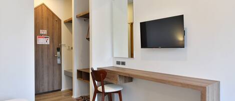 Habitación de hotel con escritorio de madera, una silla, un televisor montado en la pared y una puerta de madera.