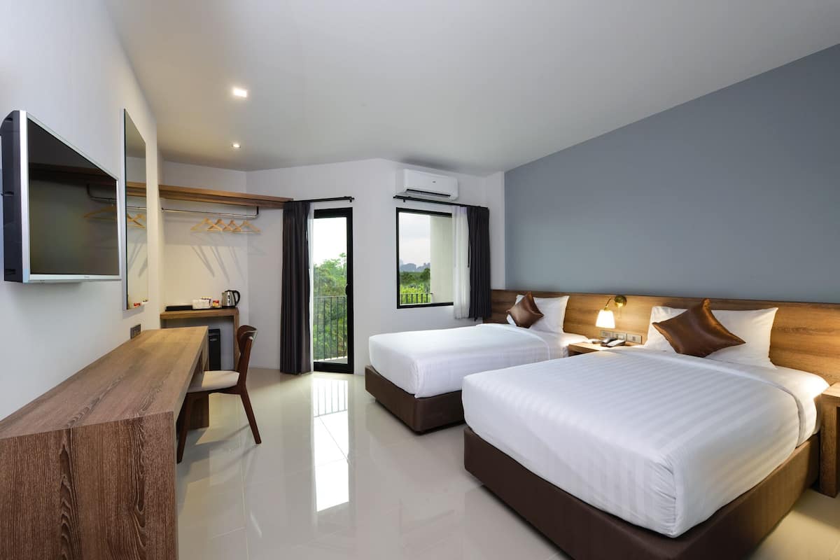A modern hotel room with two beds, a desk, a chair, and a TV.