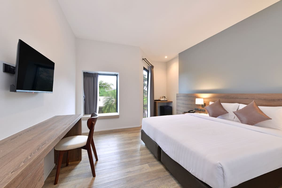 A modern hotel room with a large bed, a desk, a chair, a TV mounted on the wall, and a window with curtains.