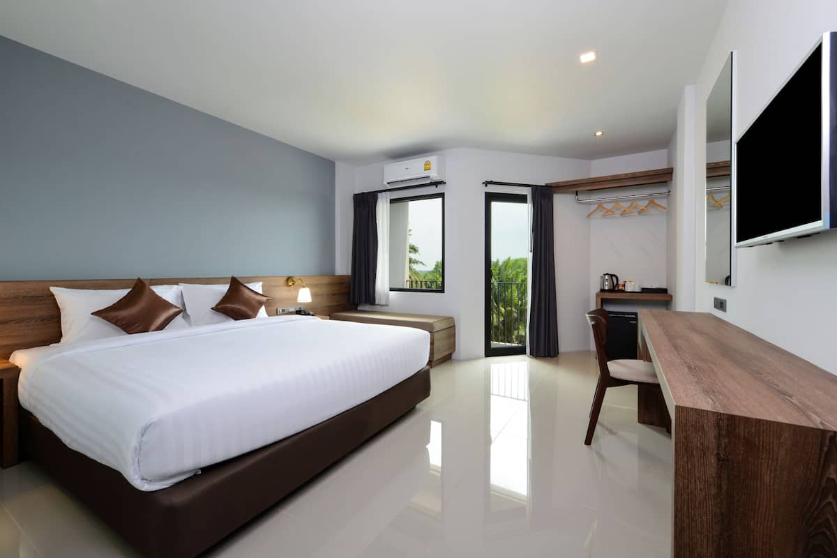 A modern hotel room with a large bed, a desk, and a view of palm trees.
