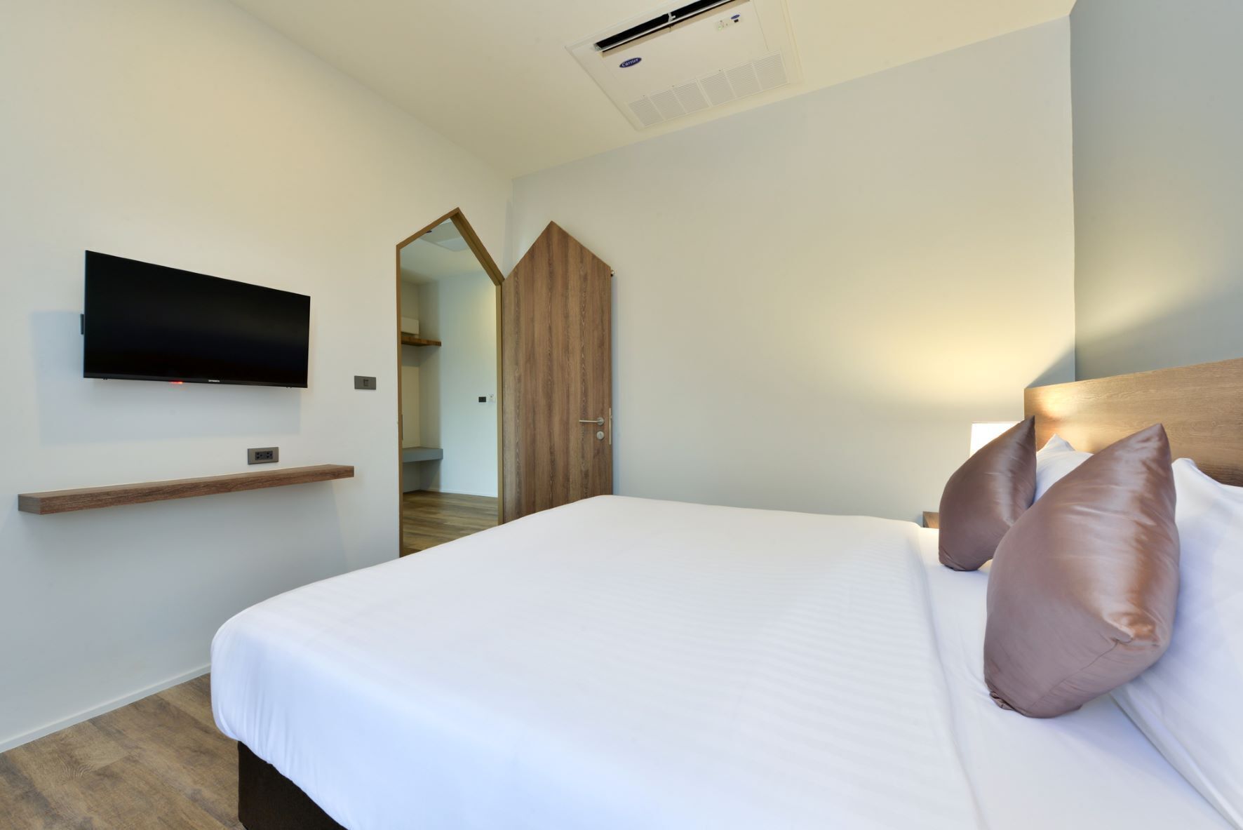 Moderni hotellihuone, jossa on suuri sänky, seinälle asennettu televisio ja puinen vaatekaappi.
