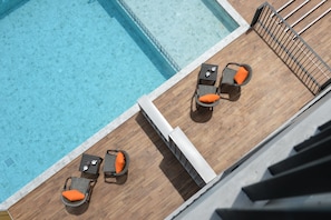A rooftop pool area with two lounge chairs and a small table, surrounded by wooden deck flooring.