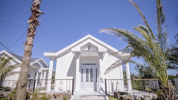 A white building with a central entrance, flanked by palm trees and surrounded by rocks.
