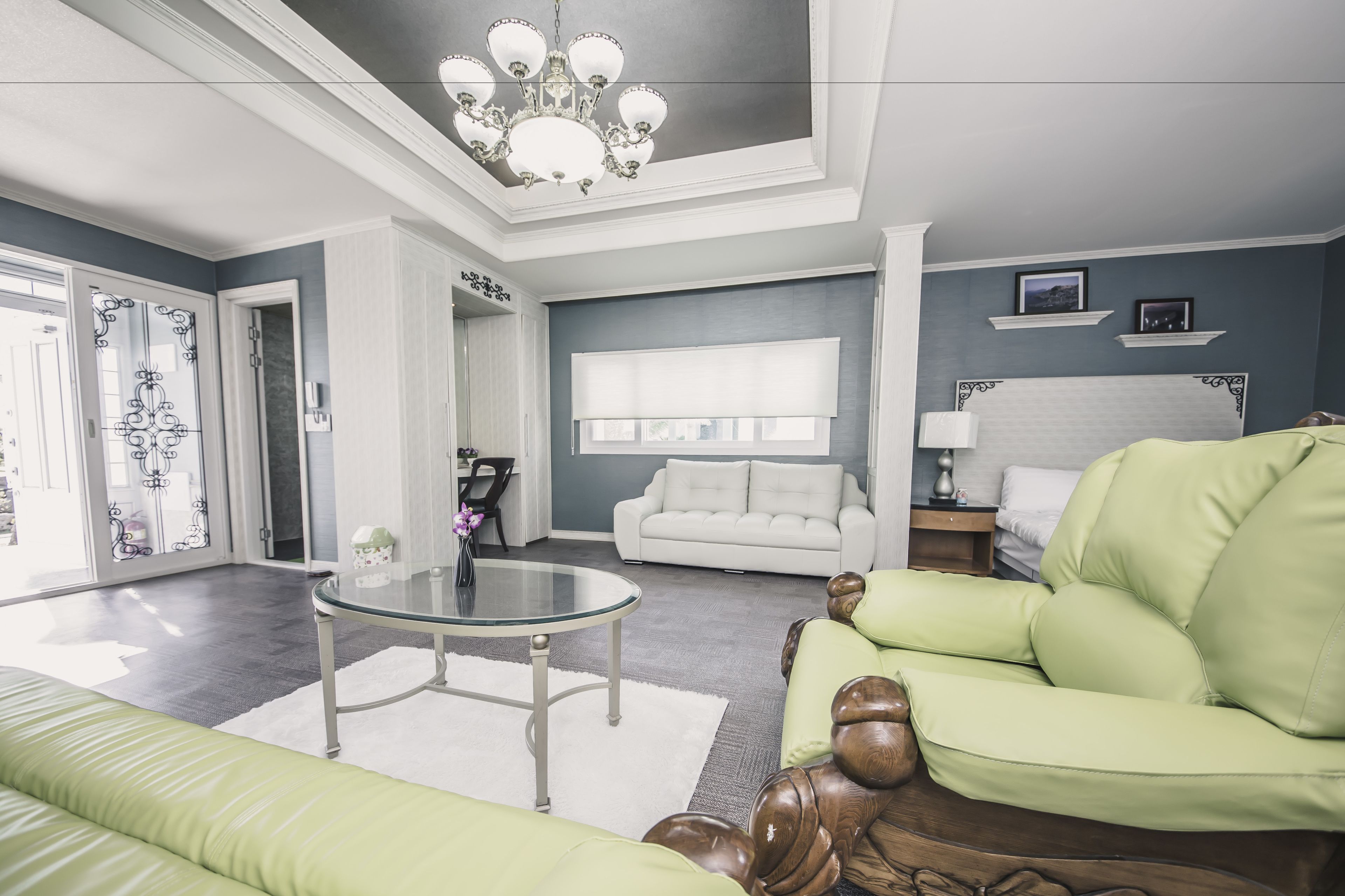Een woonkamer met een glazen salontafel, een groene bank, een witte bank en een kroonluchter.