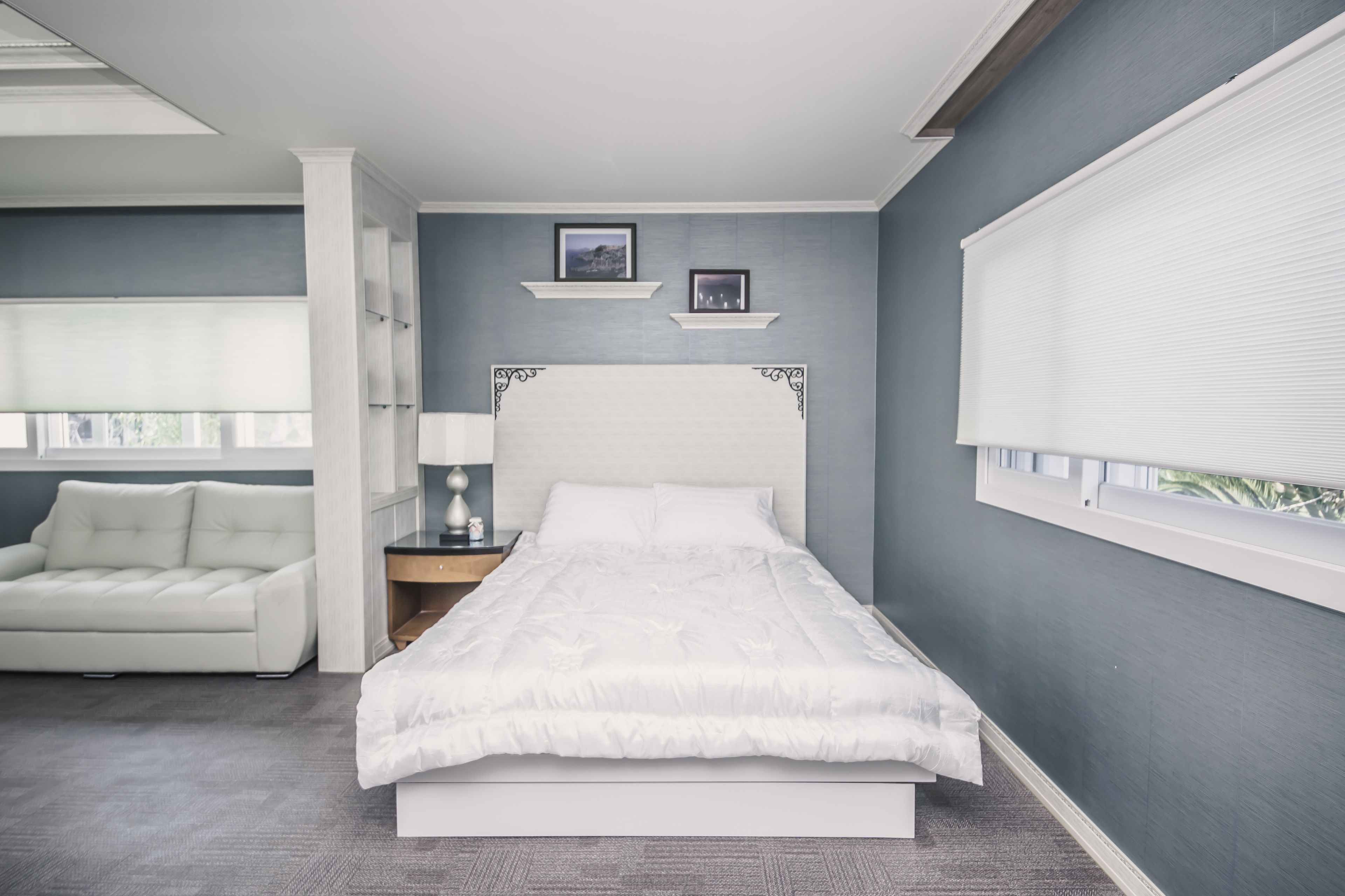 Een moderne slaapkamer met een groot bed, een nachtkastje met een lamp, een witte bank en een raam met jaloezieën.