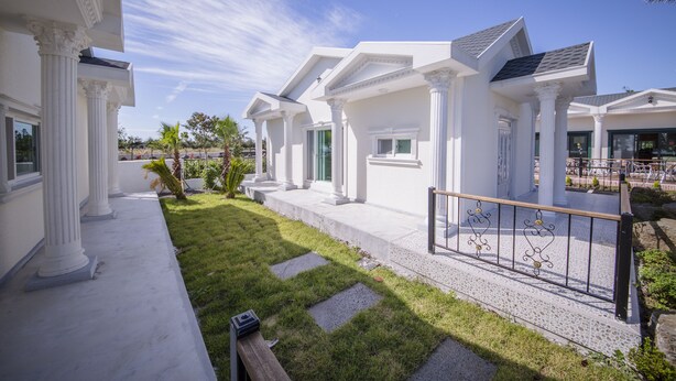 Un edificio residencial moderno con columnas blancas, un porche cubierto y un césped bien cuidado.