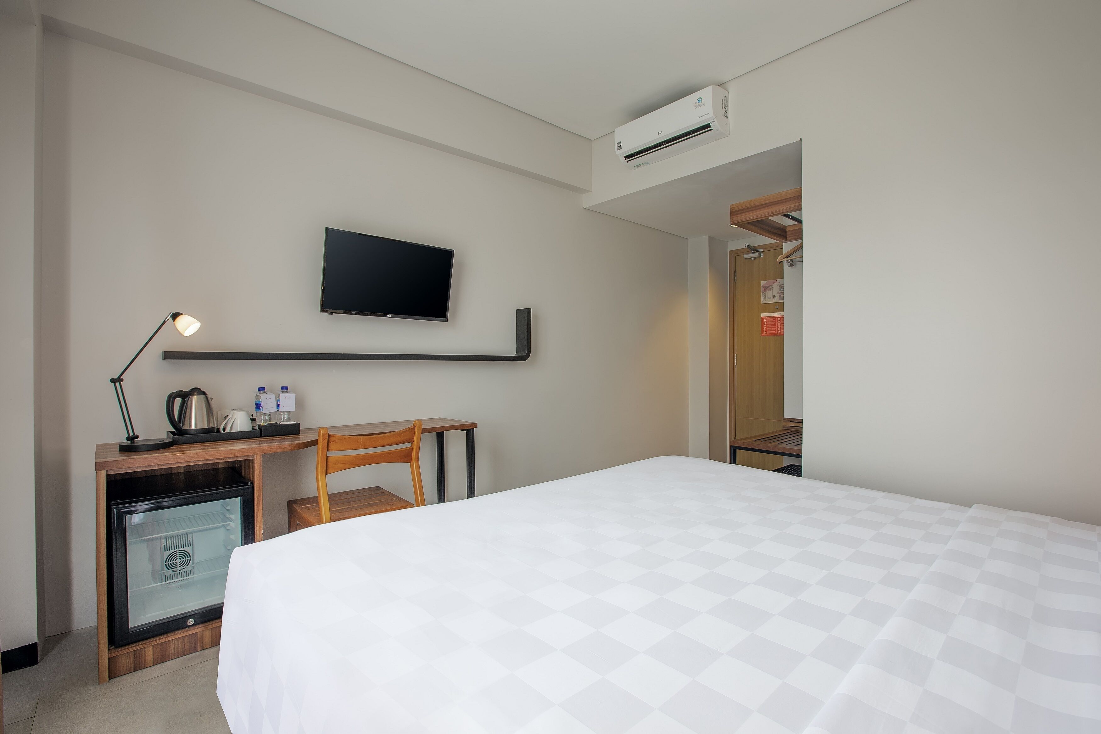 A hotel room with a bed, a desk with a lamp, a television, and an air conditioner.