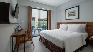 Habitación de hotel con cama, escritorio, silla, televisor y vistas al exterior.