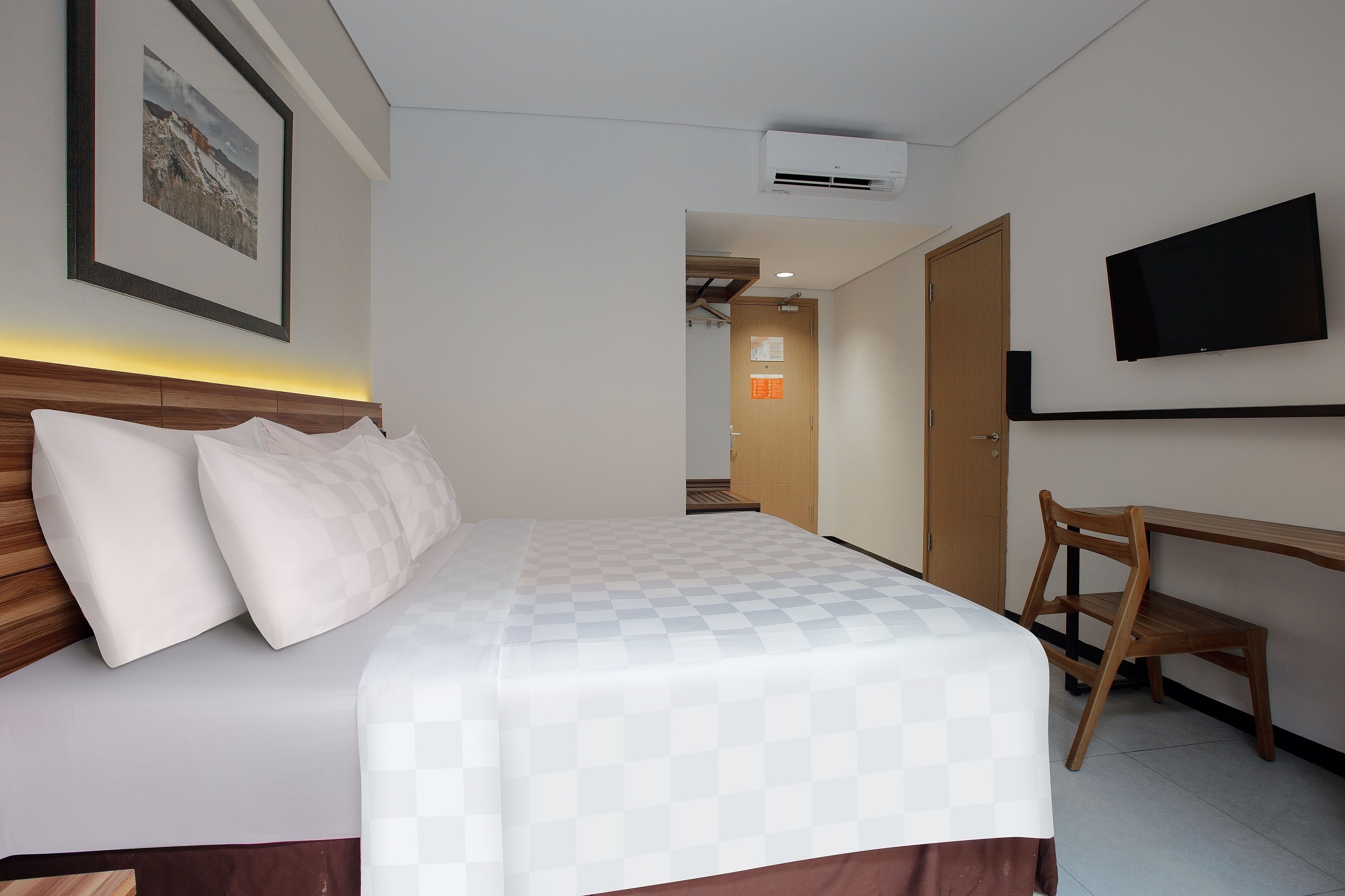 A hotel room with a bed, a desk, a chair, a television, and a framed picture on the wall.