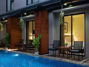 A poolside area with a blue tiled pool, wooden pillars, and black wicker chairs.