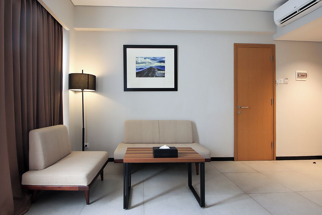 A hotel room with a sofa, a small table with a tissue box, a framed picture on the wall, a door, and an air conditioning unit.