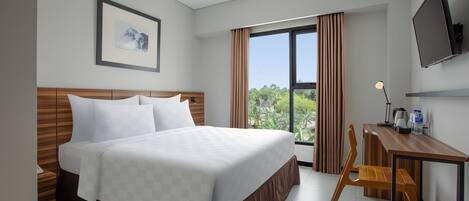 Ein Hotelzimmer mit einem großen Bett, einem Schreibtisch, einem Sessel, einem Fernseher und einem Fenster mit Vorhängen.