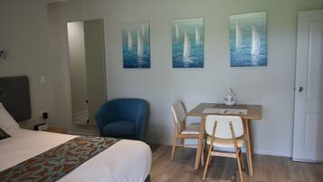 A hotel room with a bed, a desk with two chairs, and three paintings of sailboats on the wall.