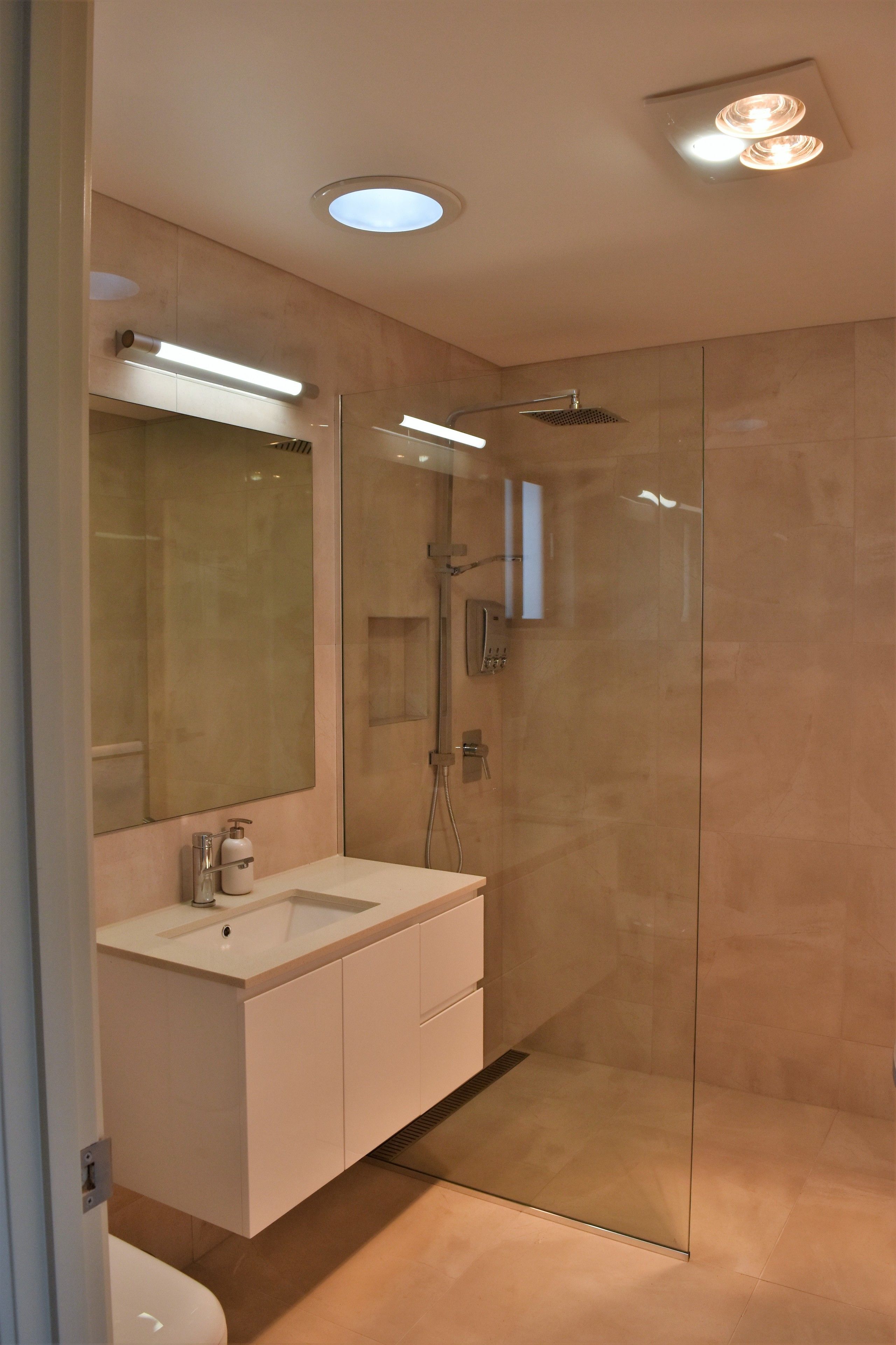 Um banheiro moderno com chuveiro em cabine de vidro, um espelho grande e um lavatório branco.