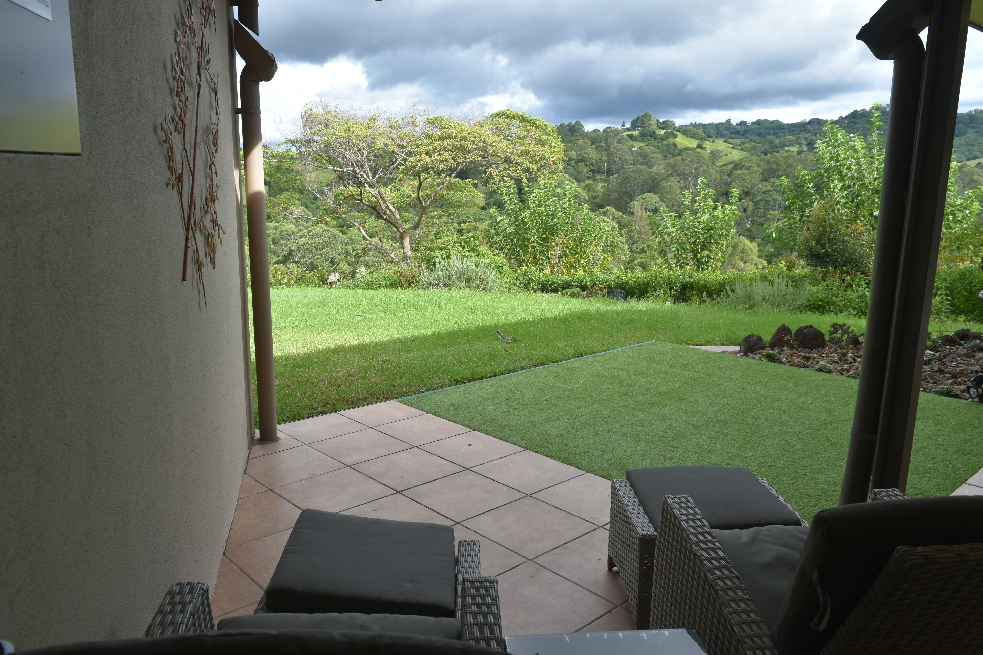A patio with wicker furniture and a view of a green lawn and trees.