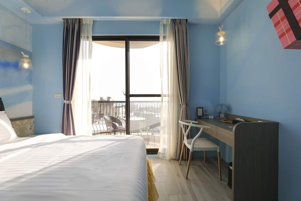 Quarto de hotel com cama, escrivaninha, cadeira e varanda com vista.