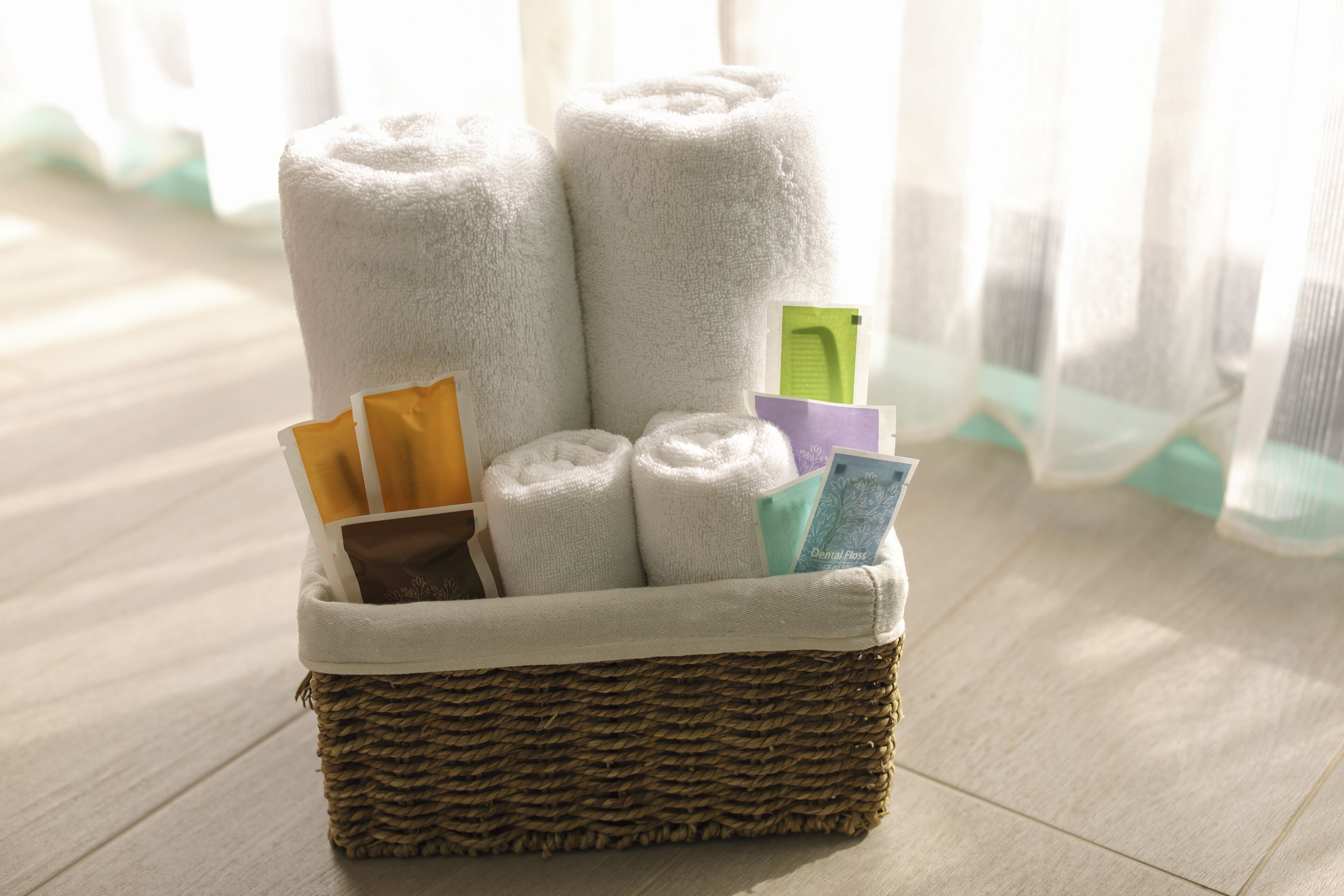 A wicker basket with rolled white towels and a few books on a wooden floor.