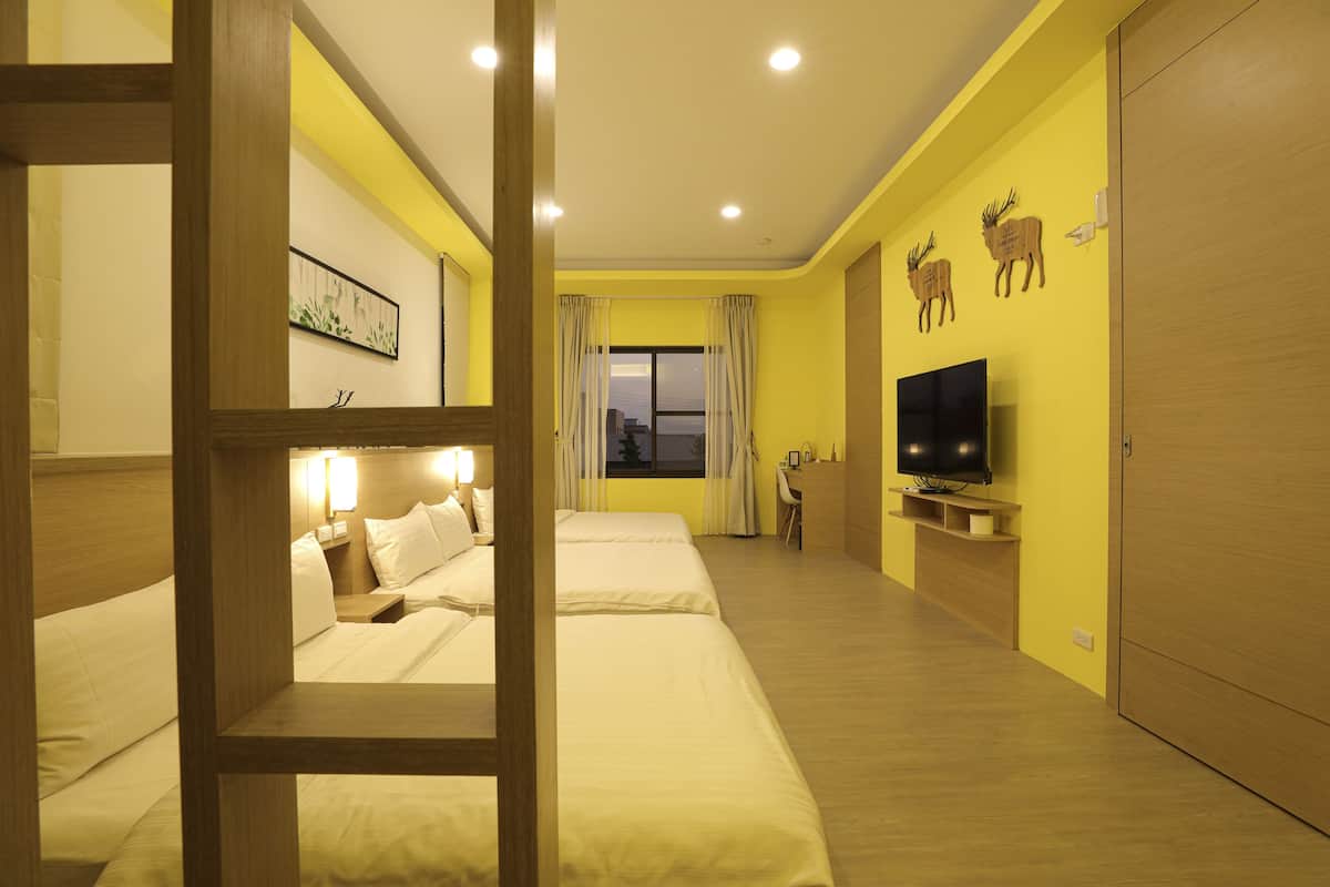 Quarto de hotel com duas camas, televisão, secretária e janela com cortinas.