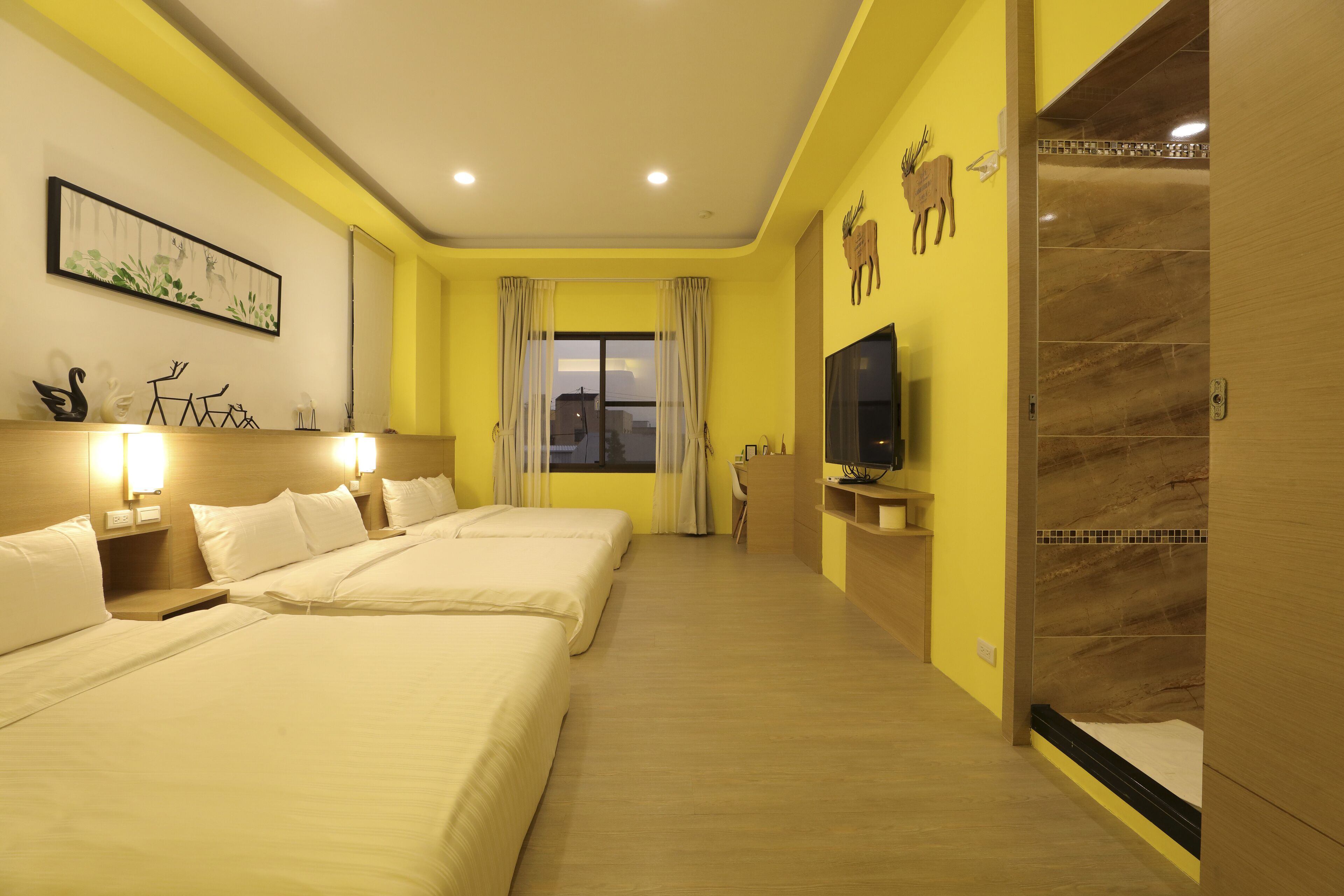 A hotel room with two beds, a TV, a desk, and a bathroom with a mirror and towel rack.