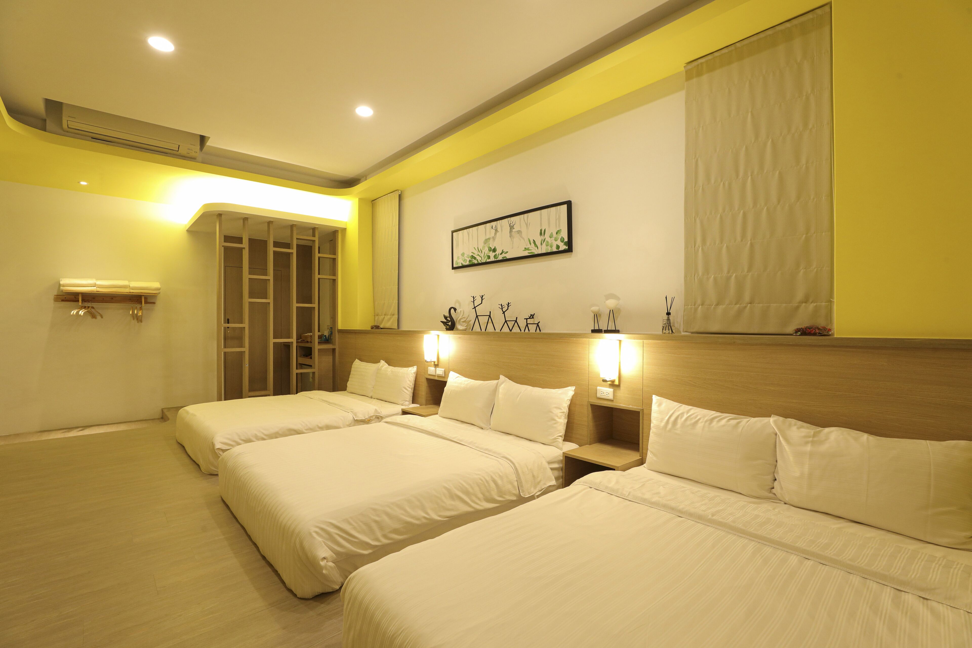 Habitación de hotel con tres camas, cabecera de madera, una obra de arte colgada en la pared y una ventana con cortina.