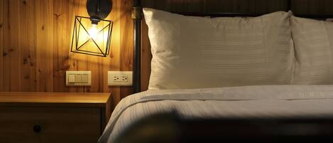 A wooden-paneled room with a bed, a nightstand, and a wall-mounted light fixture.