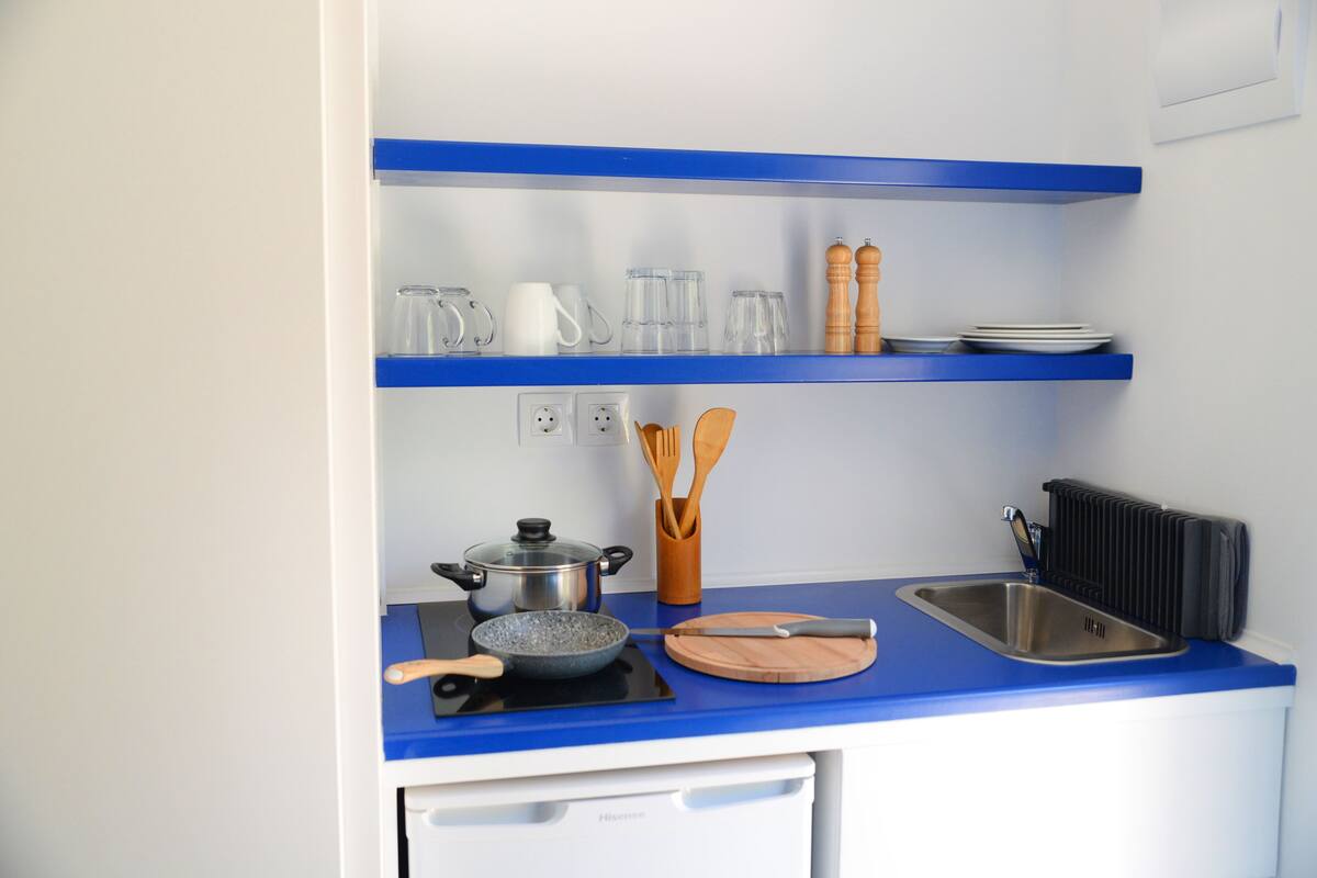 A kitchen with a blue countertop, a sink, a stove, and various kitchen utensils.