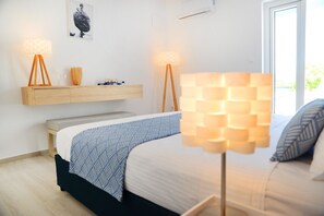 A bedroom with a bed, bedside lamps, a wooden shelf, and a window. - Aphrodite Studios (Kalymnos)