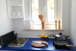 A kitchen with a blue countertop, a sink, a cutting board with a knife, a pot on an induction cooktop, and a window with a view of greenery. - Aphrodite Studios (Kalymnos)