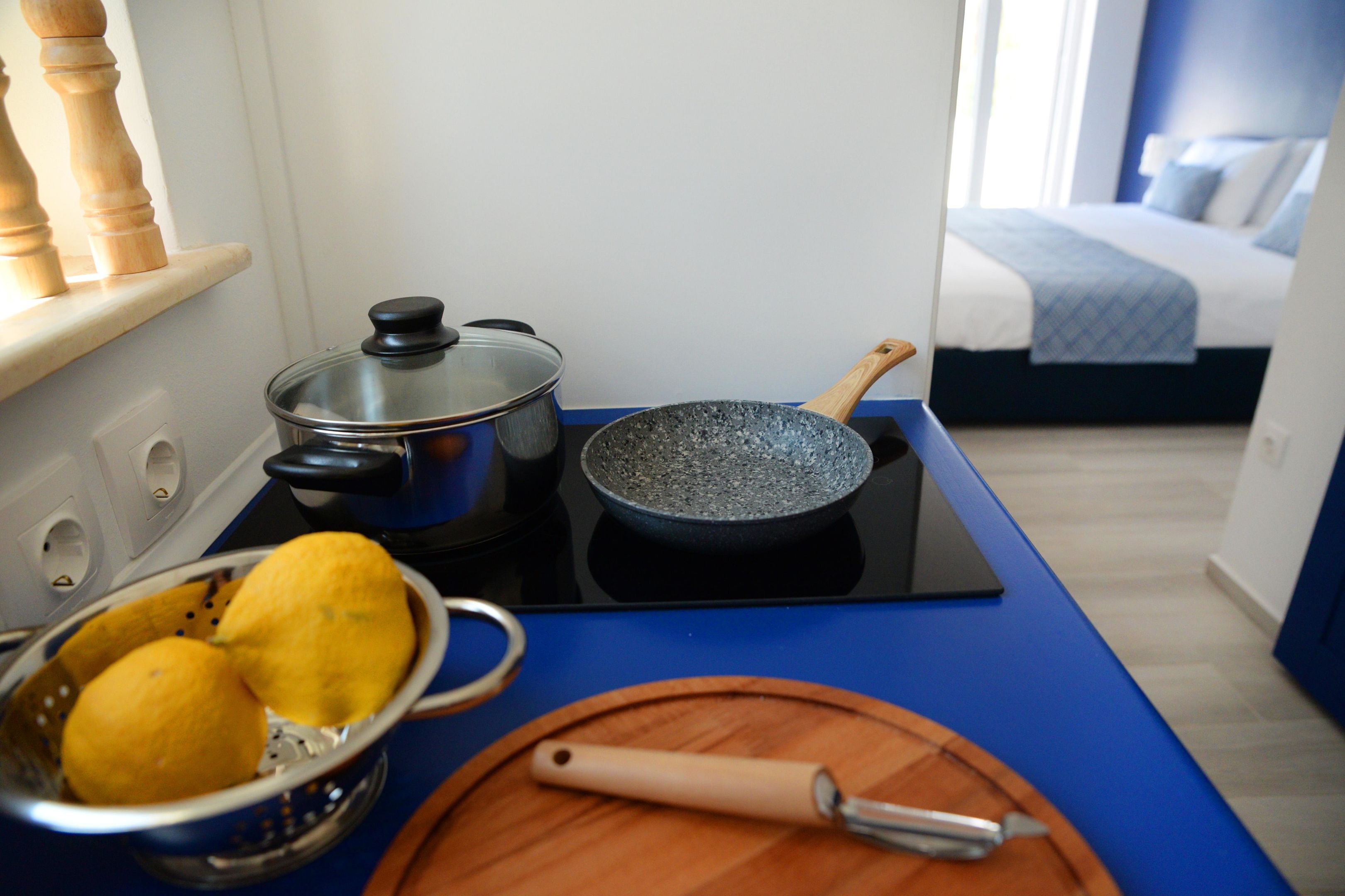 A kitchen with a stove, a frying pan, a colander with lemons, and a wooden cutting board with a knife.