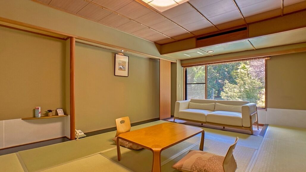 Una habitación tradicional japonesa con suelo de tatami, una mesa de madera baja, un sofá y una ventana con vistas a árboles.