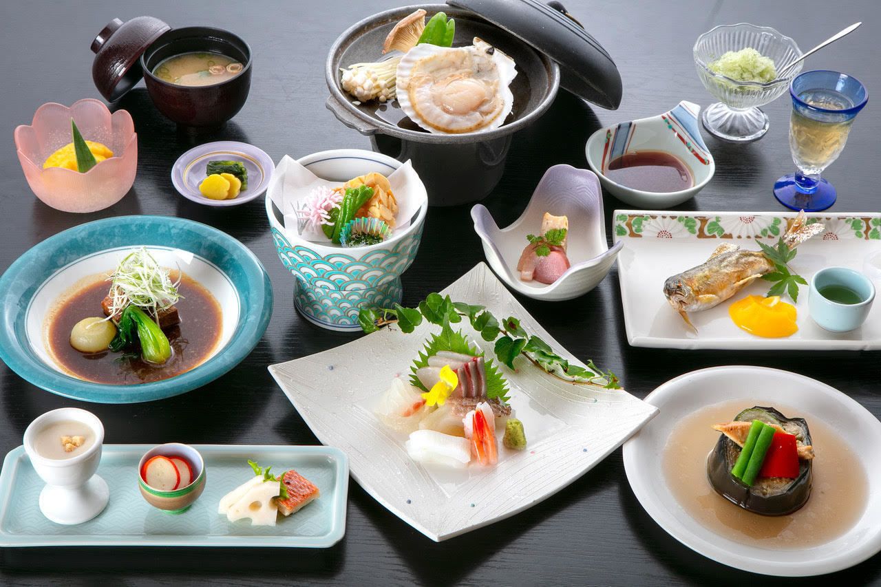 A variety of Japanese dishes arranged on a table, including a bowl of soup, a pot of seafood, and several plates with different types of food.