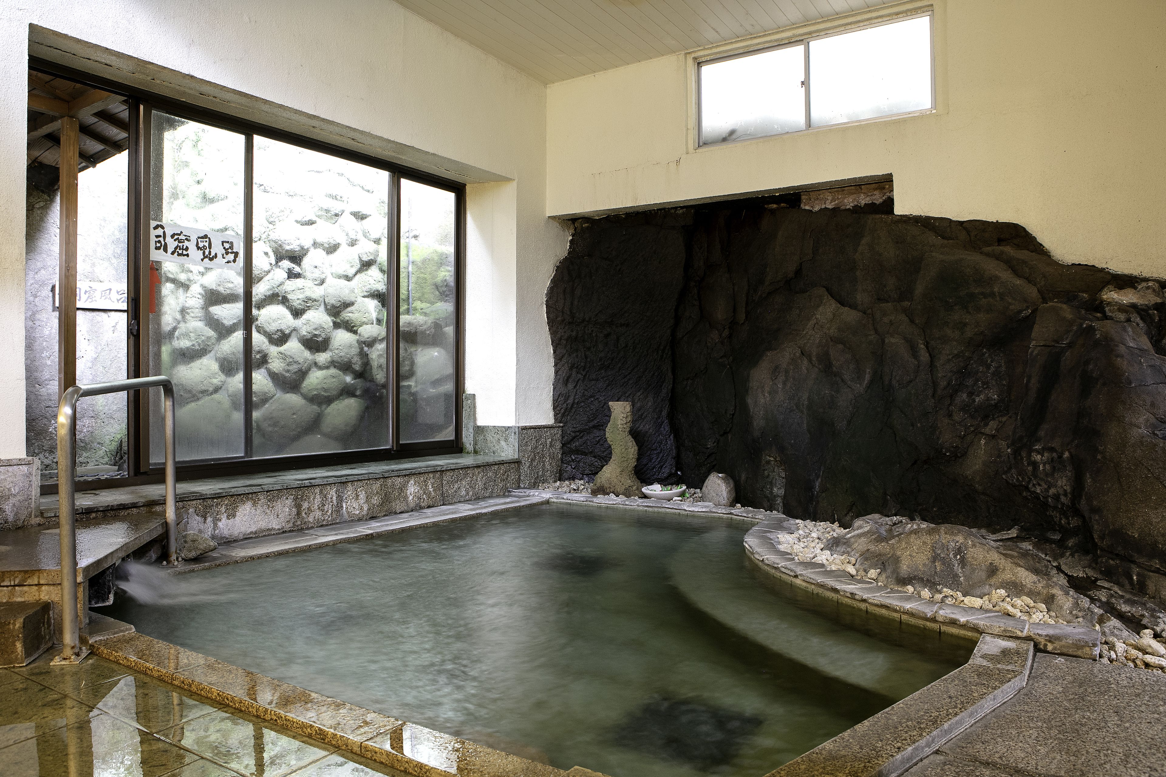 Un onsen japonés tradicional con pared de piedra, banco de madera y suelo de baldosas.
