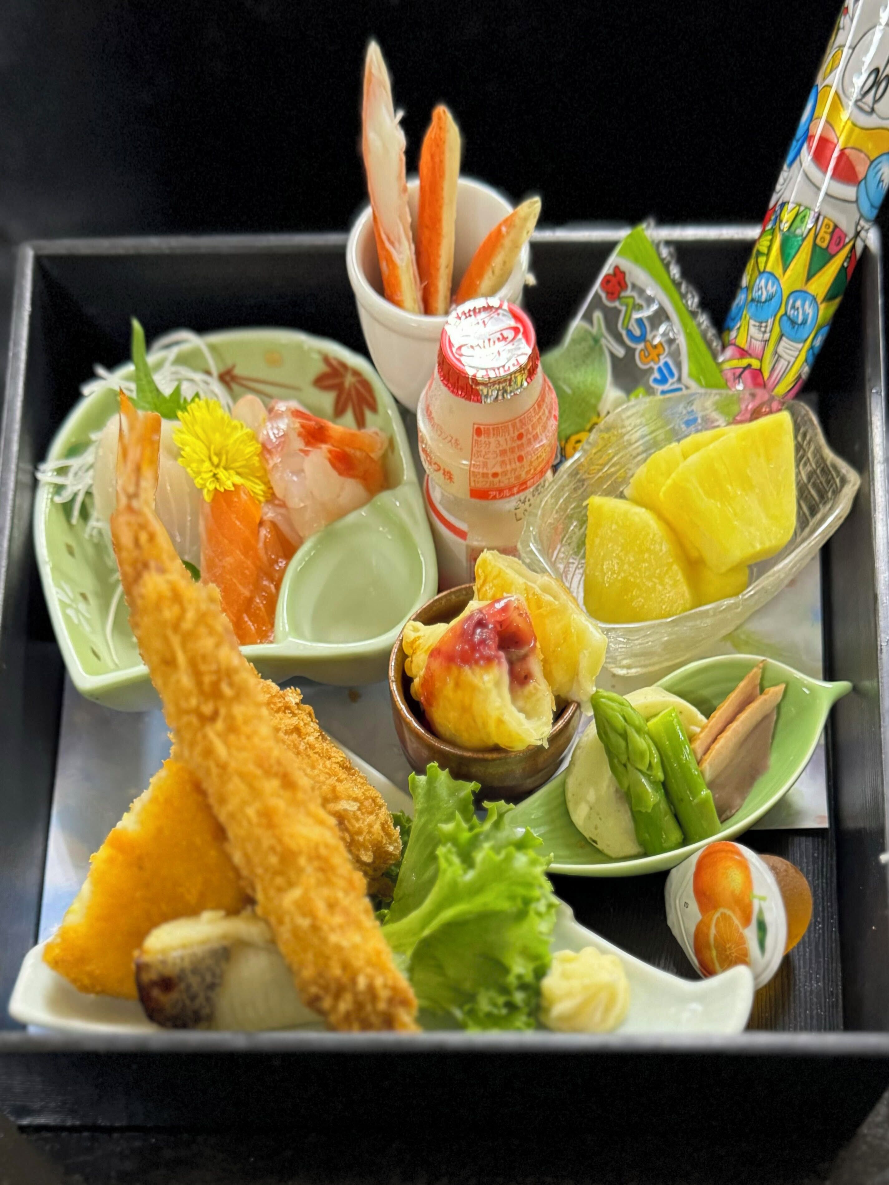 Una bandeja con diversos platillos, incluyendo sushi, sashimi y una botella de salsa.