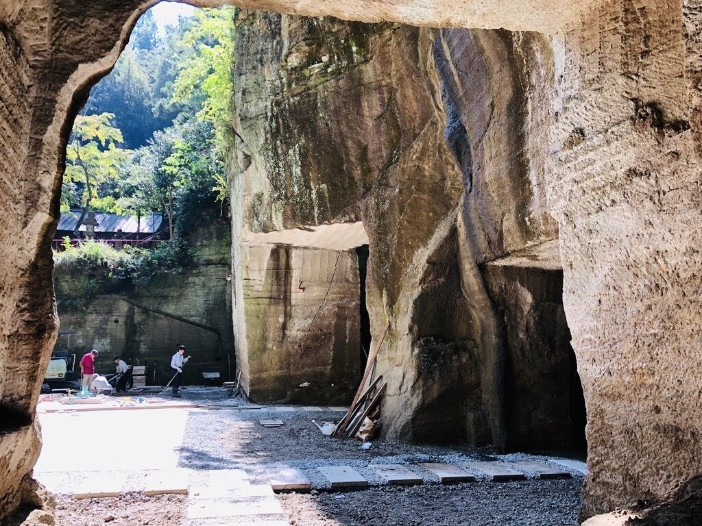 Una estructura que recuerda a una cueva, con un arco natural, una zona pavimentada y algunas personas trabajando.